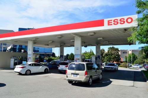 A busy Esso gas station with several cars refueling under a bright blue sky.