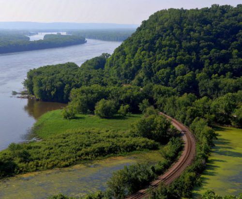 Aerial view of a winding river surrounded by lush greenery and hills under a clear sky.