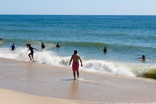 People enjoying a sunny day at the beach, playing in the waves and walking along the shore.