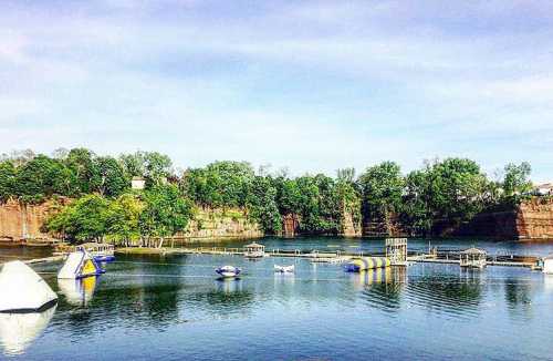 A serene lake surrounded by cliffs, featuring inflatable water toys and a wooden dock under a clear blue sky.