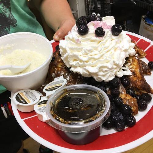 A plate of French toast topped with whipped cream and blueberries, accompanied by syrup and a side of cream.