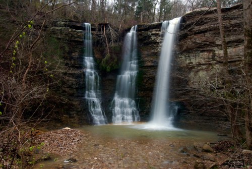 A serene waterfall cascading over rocky cliffs, surrounded by trees and a calm pool at the base.