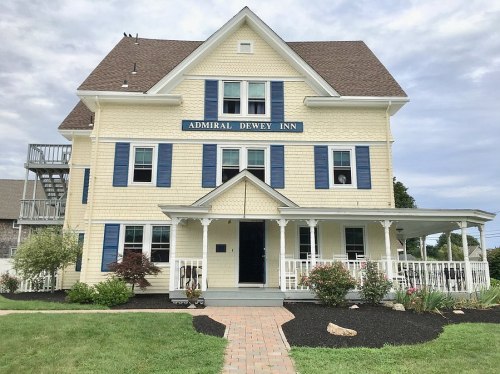 A yellow three-story inn with blue shutters and a welcoming porch, surrounded by landscaped grounds.