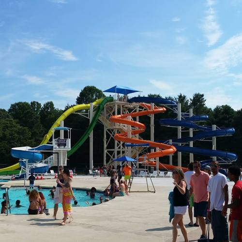 A busy water park with colorful slides, a pool, and people enjoying the sunny day.