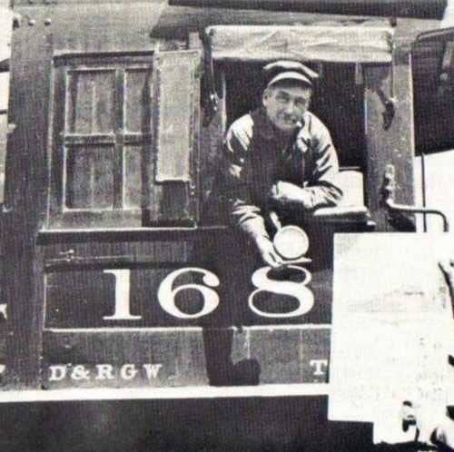 A vintage black and white photo of a train engineer leaning out of a locomotive window, holding a lantern.