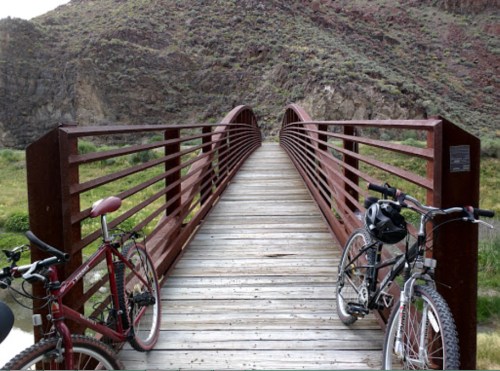 Two bicycles parked on a wooden bridge surrounded by rocky terrain and greenery.