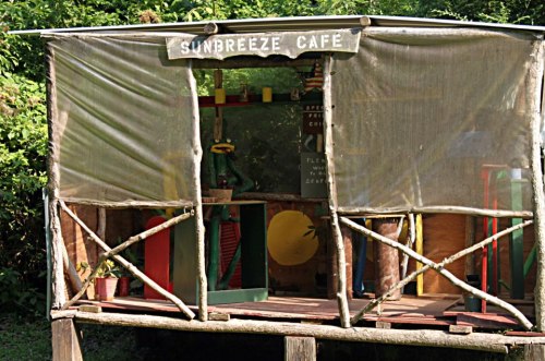 A rustic café structure with a sign reading "Sunbreeze Café," surrounded by greenery and wooden supports.