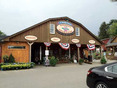 A rustic market building with signs for bakery, deli, produce, and gifts, decorated with bunting and surrounded by plants.