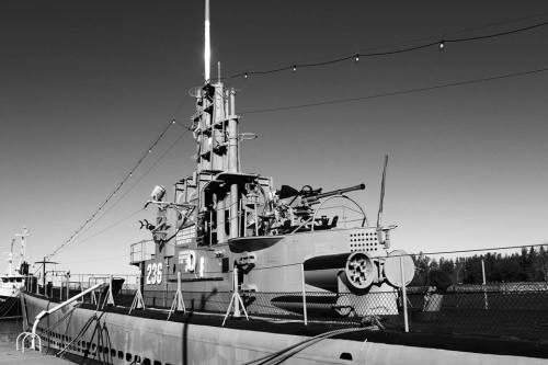 A black and white image of a vintage submarine docked, with crew members and equipment visible on the deck.