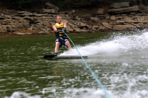 A person water skiing on a lake, creating a spray of water behind them as they glide across the surface.