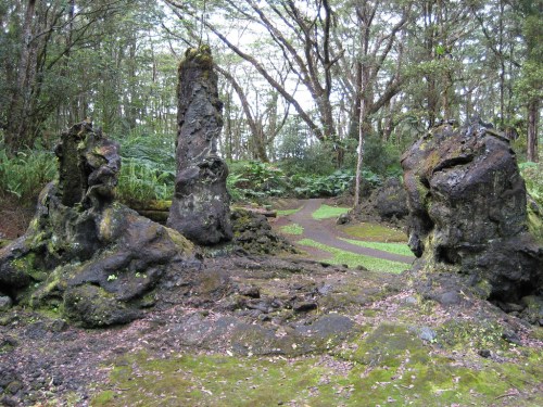 Two tall, dark rock formations surrounded by lush greenery in a forested area.