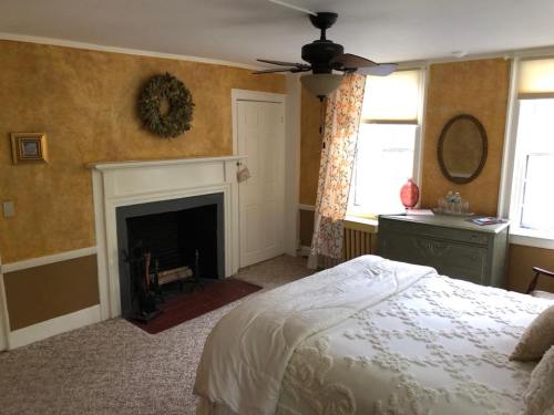 Cozy bedroom with a fireplace, yellow walls, a bed, and a vintage dresser, featuring natural light from windows.