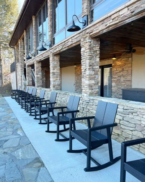 A row of black rocking chairs on a stone patio in front of a rustic building with large windows.