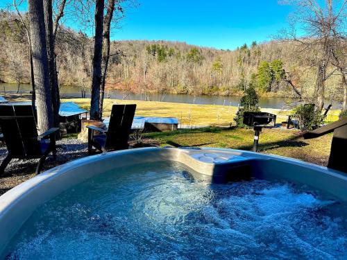 A hot tub with bubbling water overlooks a serene river and wooded landscape on a clear day.