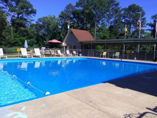 A clear blue swimming pool surrounded by lounge chairs and a shaded area, with trees and flags in the background.