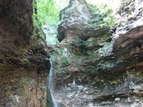 A serene waterfall cascading down rocky cliffs, surrounded by lush greenery and natural rock formations.