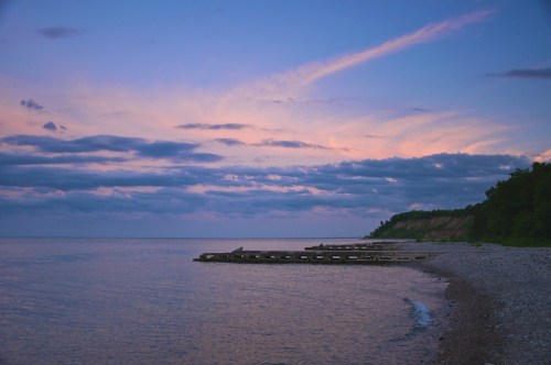 A serene lakeside view at dusk, featuring a wooden dock and colorful clouds reflecting on the water.