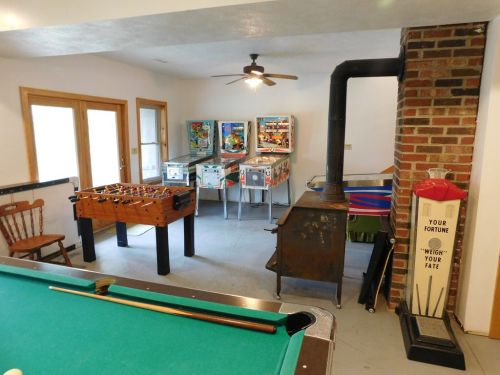 A game room featuring a pool table, foosball table, pinball machines, and a vintage fortune teller machine.