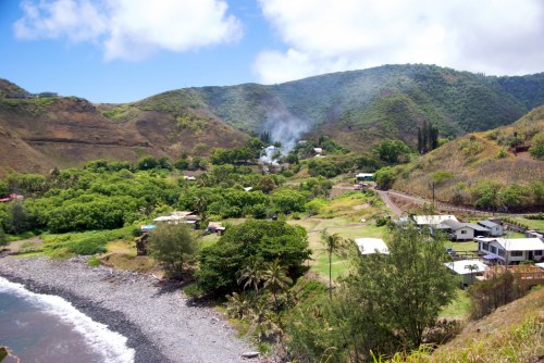 A scenic view of a coastal village surrounded by lush hills and greenery, with a clear blue sky above.