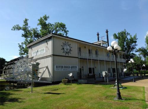 A riverside building with a paddlewheel, featuring a sign that reads "River Road Queen" and surrounded by green grass.