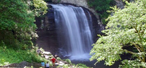 A scenic waterfall surrounded by lush greenery, with people admiring the view nearby.