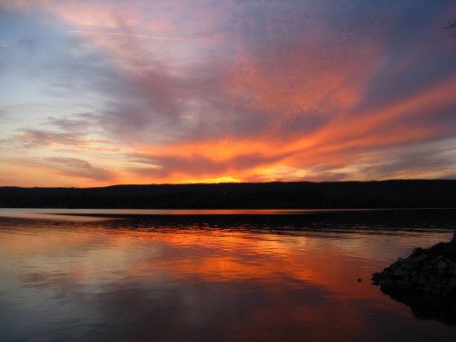 A vibrant sunset over a calm lake, with colorful clouds reflecting on the water's surface.