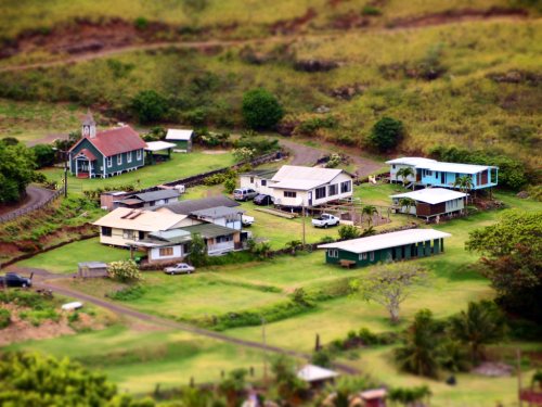 Aerial view of a small village with several houses, a church, and green fields surrounding them.