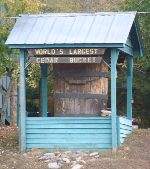 A large wooden bucket displayed under a blue shelter, labeled "World's Largest Cedar Bucket."
