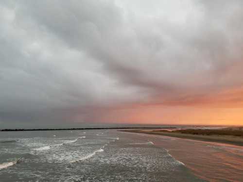 A serene beach scene at sunset, with dark clouds and gentle waves lapping at the shore.