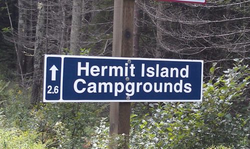 Sign for Hermit Island Campgrounds, indicating a distance of 2.6 miles, surrounded by trees.