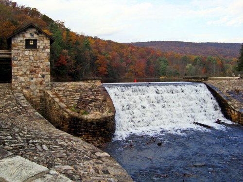 A stone dam with a waterfall, surrounded by autumn foliage and a serene river landscape.