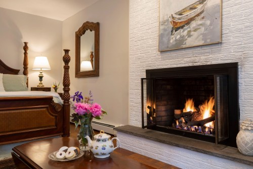 Cozy room with a fireplace, floral arrangement, and a bed in the background, creating a warm, inviting atmosphere.