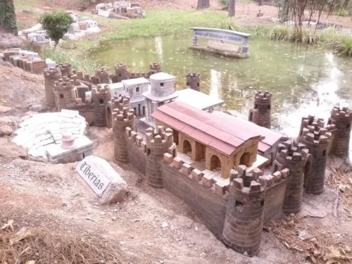 A miniature castle and structures by a pond, surrounded by greenery, showcasing intricate architectural details.