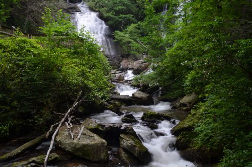A serene waterfall cascades down rocky terrain, surrounded by lush green trees and flowing water.