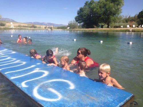 A group of children swimming in a clear lake, with an adult supervising them near a blue platform labeled "swimming."