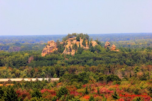 A rocky outcrop surrounded by lush green trees, with hints of autumn colors in the foliage below.