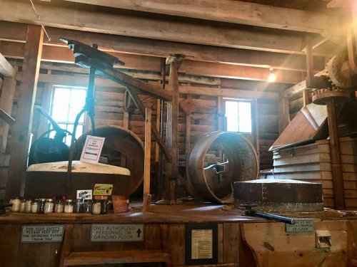 Interior of a rustic wooden building featuring vintage machinery and equipment, with sunlight streaming through windows.