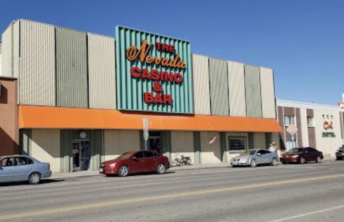 Exterior of The Nevada Casino & Bar, featuring a green and orange facade, with cars parked in front on a sunny day.