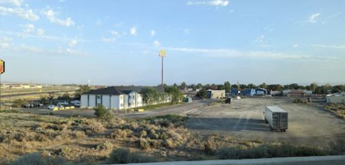 A view of a McDonald's sign near a parking lot and several buildings in a sparse, open area under a clear sky.
