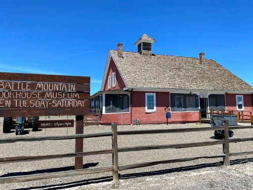 A red and white building with a peaked roof, labeled "Battle Mountain Bookhouse Museum," surrounded by a wooden fence.