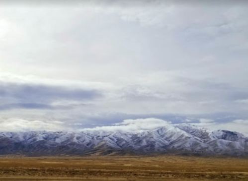Snow-capped mountains under a cloudy sky, with a vast, barren landscape in the foreground.