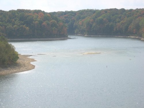A serene lake surrounded by trees with autumn foliage, reflecting the sky and gentle ripples on the water's surface.