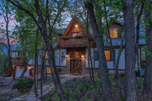 A charming house surrounded by trees, featuring a wooden entrance and warm lights, set in a serene outdoor environment.