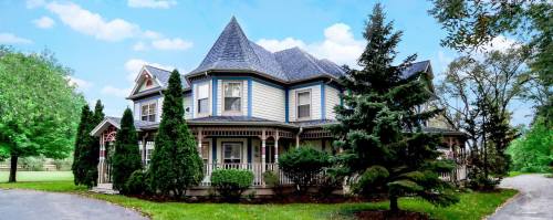 A charming Victorian-style house with a turret, surrounded by lush greenery and trees under a blue sky.