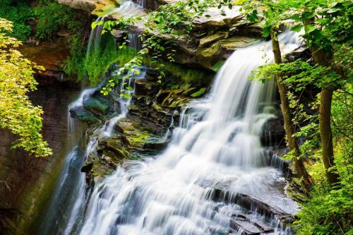 A serene waterfall cascading over rocky cliffs, surrounded by lush green foliage and trees.