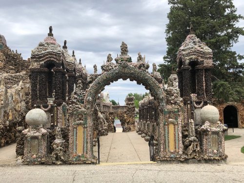A decorative archway made of colorful stones and sculptures, leading into a unique, artistic outdoor space.