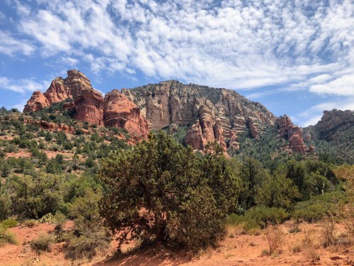 A scenic view of red rock formations and green vegetation under a partly cloudy sky.