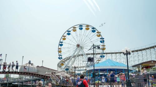 A bustling amusement park scene featuring a large Ferris wheel and a roller coaster under a clear sky.