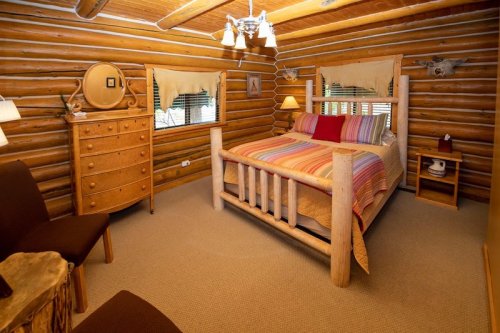 Cozy log cabin bedroom featuring a wooden bed, dresser, and warm lighting, with rustic decor and a comfortable atmosphere.