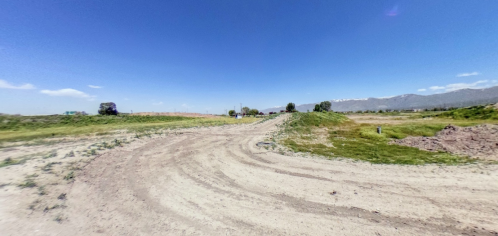 A dirt path winds through a grassy landscape under a clear blue sky, with distant mountains in the background.